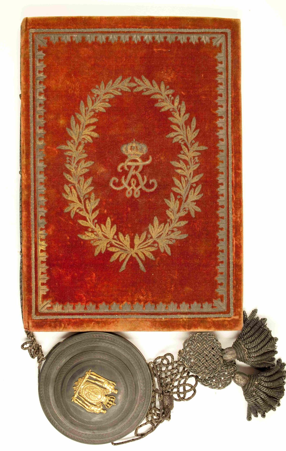 Das Bild zeigt die Urkunde mit rotem Samteinband und prachtvoller Siegelkapsel aus Metall. Daran hängt eine große Kordel.