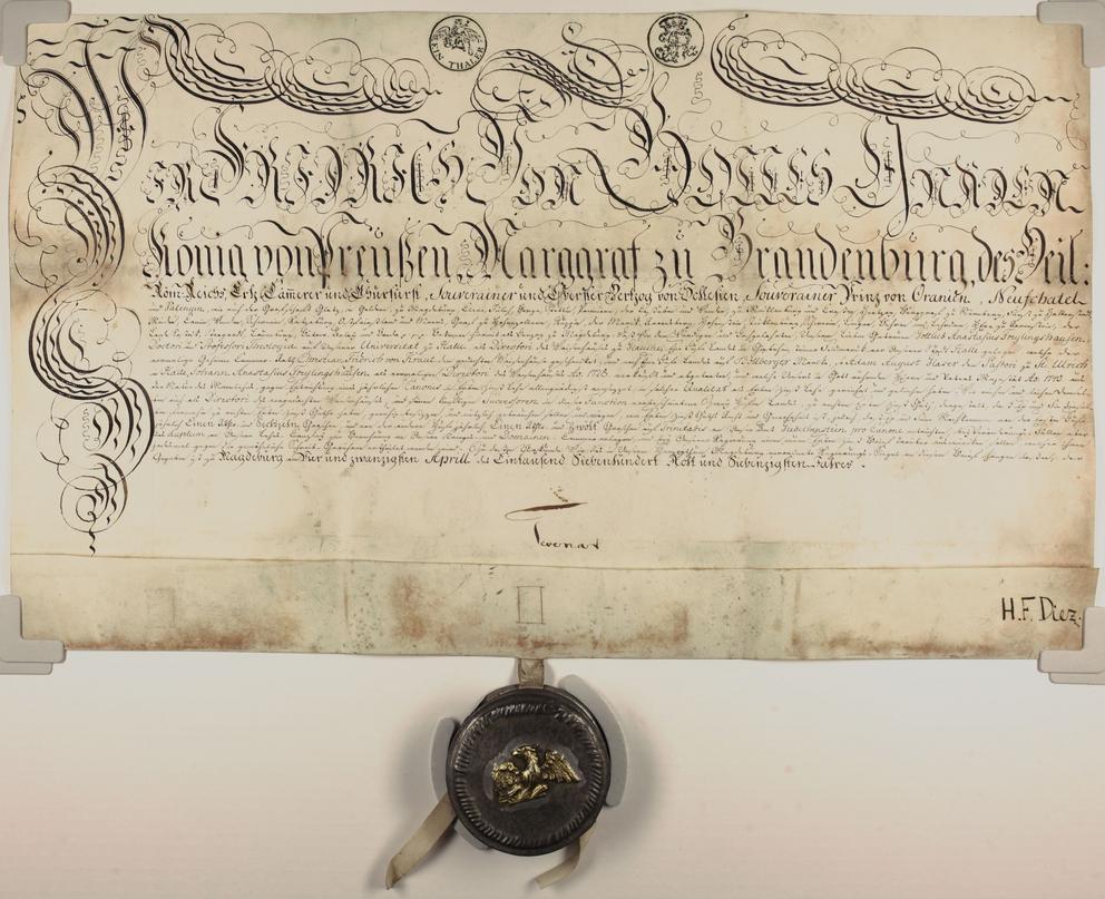 Das Bild zeigt die Pergamnenturkunde mit Auszeichnungsschrift und der Siegelkapsel aus Metall. Darauf ist der preußische Adler in Gold zu sehen.